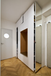 Šatní skříň spojená s botníkem kombinuje bílou barvu s bukovou překližkou v nice a nerezovým plechem na sezení. (Rekonstrukce bytu ve Vršovicích, Amulet architekti)