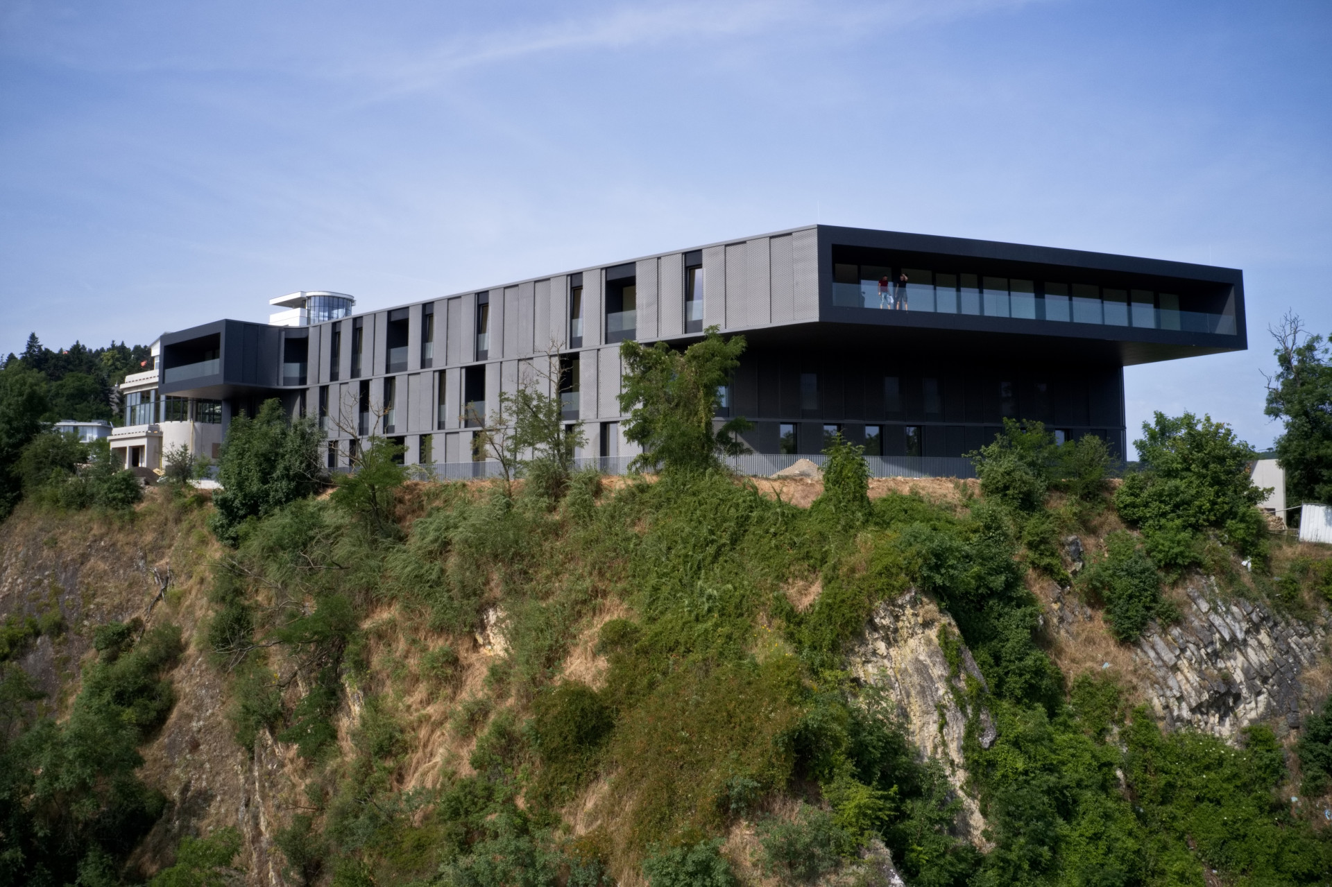 Větší dům má čtyřicet pět bytů, má tmavou kovovou fasádu a půdorys lichoběžníku. Podle architektů má kontrastovat s oblou bílou vlnovkou.