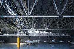 "Sloupy po obvodu nesou dvě osnovy 24 m a 18 m dlouhých nosníků. Obě tyto osnovy se potkávají asymetricky. Ve směru této osy je pnut nejvyšší a nejvíce zatížený nosník celé konstrukce, který je podepřen jedním, zmíněným sloupem. " popisují řešení architekti. (Hangár ve Zbraslavicích, Studio Raketoplán)