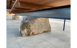 Pod střechou je umístěn dlouhý dřevěný stůl s dvěma lavicemi. Ty jsou podepřeny kameny z nedalekého lomu. (Zahrada Hage, Brendeland & Kristoffersen)