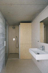 Velká společná koupelna  v přízemí. Horká pára se setkává s betonovými tvárnicemi na stěně místnosti. Dřevěný obklad vestavěné skříně vyvažuje strohost betonu útulností. (Rodinný dům v Radotíně, Papundekl architekti)