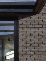 Fasáda domu je obložená tmavými cihelnými pásky. (Rodinný dům v Řepích, Stempel & Tesař architekti)