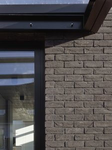 Fasáda domu je obložená tmavými cihelnými pásky. (Rodinný dům v Řepích, Stempel & Tesař architekti)