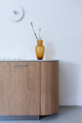 Kolem zaoblené stěny se vine na míru vyrobená dřevěná skříň s betonovou deskou.