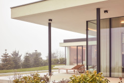 Černé subtilní rámy prosklených exteriérových stěn a štíhlé nosné sloupy dodávají stavbě jemnou dynamiku a elegantní kontrast k přírodním tónům fasády a okolní zahrady. (Bungalov ve východních Čechách; Atelier Kunc)