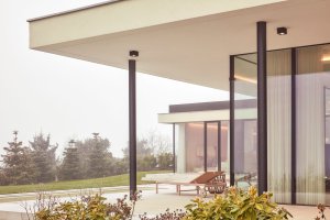 Černé subtilní rámy prosklených exteriérových stěn a štíhlé nosné sloupy dodávají stavbě jemnou dynamiku a elegantní kontrast k přírodním tónům fasády a okolní zahrady. (Bungalov ve východních Čechách; Atelier Kunc)
