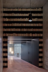 Obnova Červeného kostela, atelier-r: Rozsáhlé stěny vyplněné starými knihami otočenými hřbety dozadu s večerním podsvícením