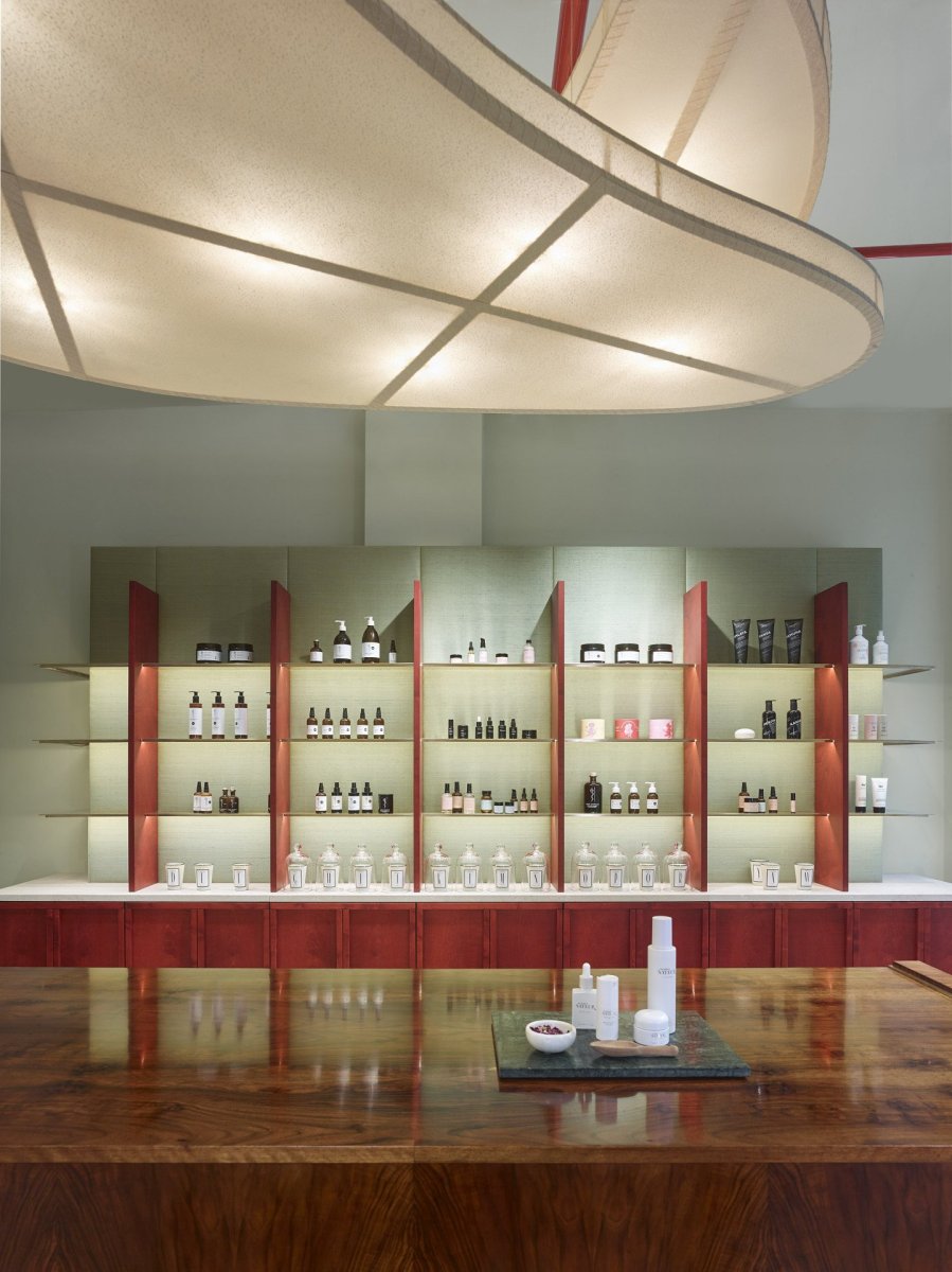 Showroom kosmetiky v Karlíně, P E T R I K + K O T R C & Nora Sopková: Horizontálně orientovaný regál má sokl a stojny jednotlivých polic namořeny do rudě červeného odstínu