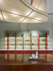 Showroom kosmetiky v Karlíně, P E T R I K + K O T R C & Nora Sopková: Horizontálně orientovaný regál má sokl a stojny jednotlivých polic namořeny do rudě červeného odstínu