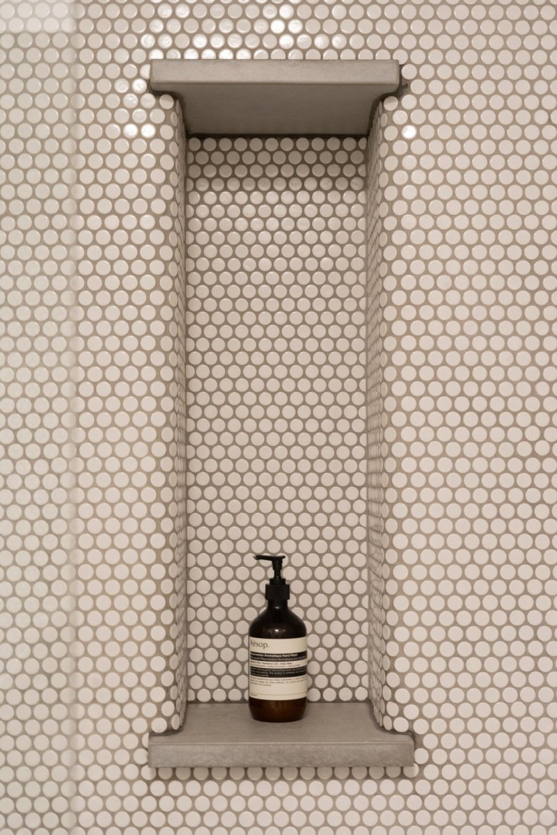 Bílý obklad doplňují mosazné baterie a niky s betonovými deskami. (rekonstrukce prvorepublikového bytu v Bubenči, Studio COSMO)