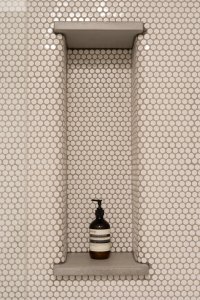Bílý obklad doplňují mosazné baterie a niky s betonovými deskami. (rekonstrukce prvorepublikového bytu v Bubenči, Studio COSMO)
