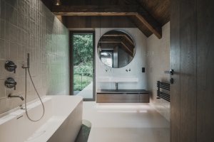 Koupelna kombinuje současné materiálové řešení s přiznaným krovem a výhledy do okolní krajiny. (Chalupa ve stráni; Mimosa Architekti)