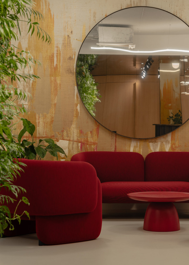 Kulaté zrcadlo nad pohovkou odráží dřevěný obklad recepce a rozšiřuje úzký prostor lounge. (Kanceláře JSK v Praze; BekArch)