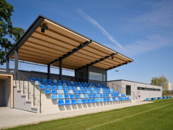 Divácká tribuna je krytá vykonzolovanou dřevěnou střechou, pod kterou je také kabina hlasatele s dobrým výhledem na celé fotbalové hřiště. (Sportovní areál SK Planá, PROAM ARCHITEKTI)
