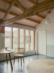 Komunitní centrum s ubytováním Waxall Yard, Clementine Blakemore Architects: Obnažené dřevěné nosníky střechy a cihly v kombinaci s dřevěným nábytkem a prvky světlých barevných odstínů dodávají interiérům příjemnou atmosféru místa mimo dnešní uspěchaný svět, kde se zastavil čas