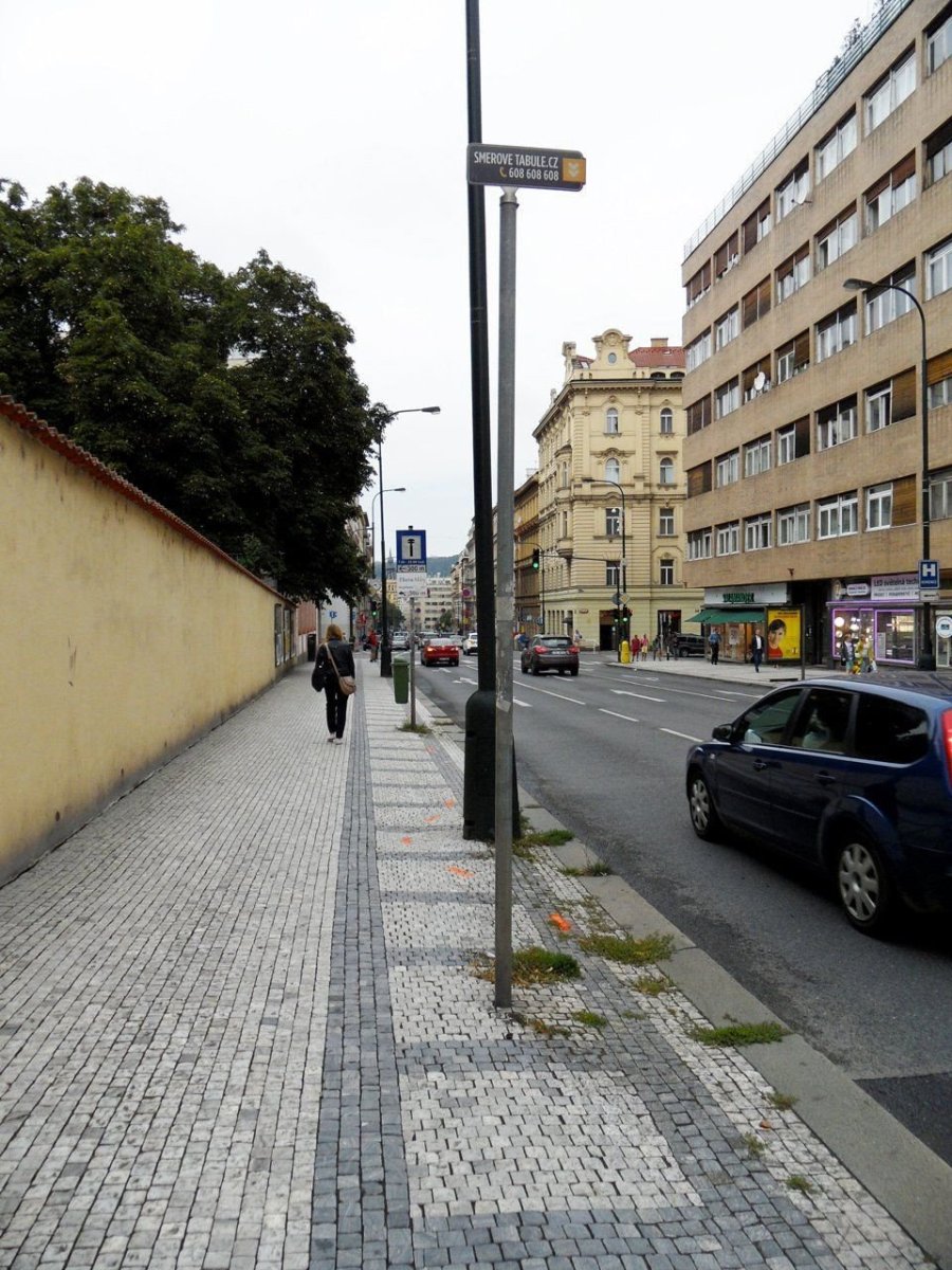 Praktičnost: Proč město povoluje umístění sloupků omezujících pohyb po chodníku v místě, kde vše důležité může být připevněno na stožáry veřejného osvětlení? Čtvrt chodníku jedné z nejrušnějších pražských ulic kvůli tomu nikdo nemůže používat ani uklízet, a tak mezi dlažbou roste tráva. / Žitná ulice v Praze – foto