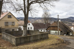 Další památkou obci Strašín je žulová kašna, roubenka v pozadí. (Roubená chalupa Strašín)