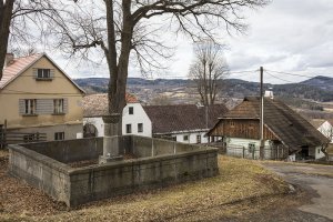 Další památkou obci Strašín je žulová kašna, roubenka v pozadí. (Roubená chalupa Strašín)