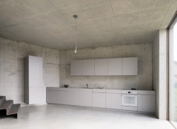 Betonové zdi, světlá kuchyně a kovové schodiště vytváří neutrální kulisu. (Rodinný dům nedaleko Olomouce, studio Malý Chmel)