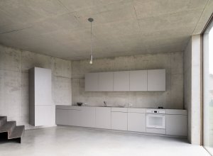 Betonové zdi, světlá kuchyně a kovové schodiště vytváří neutrální kulisu. (Rodinný dům nedaleko Olomouce, studio Malý Chmel)