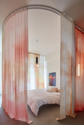 Ty mají taky užitnou funkci, splývají kolem postele a oddělují tak spací zónu, do které propouštějí jemně zabarvené světlo. (Byt v Praze, ateliér Malfino)