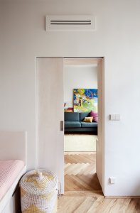 Příčka mezi obytným prostorem a ložnicemi již byla. Architekta do ní pouze navrhla více otvorů, pouzdra posuvných dveři a schovala ji za knihovnu. (Rekonstrukce bytu na Vinohradech, Markéta Bromová architekti)