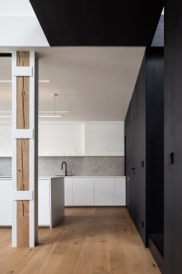 Půdní byt s černým boxem, Komon architekti: Nosné sloupy uprostřed dispozice mimo své hlavní funkce posloužili ještě k dalšímu účelu. Autoři mezi ně umístili promítací plátno