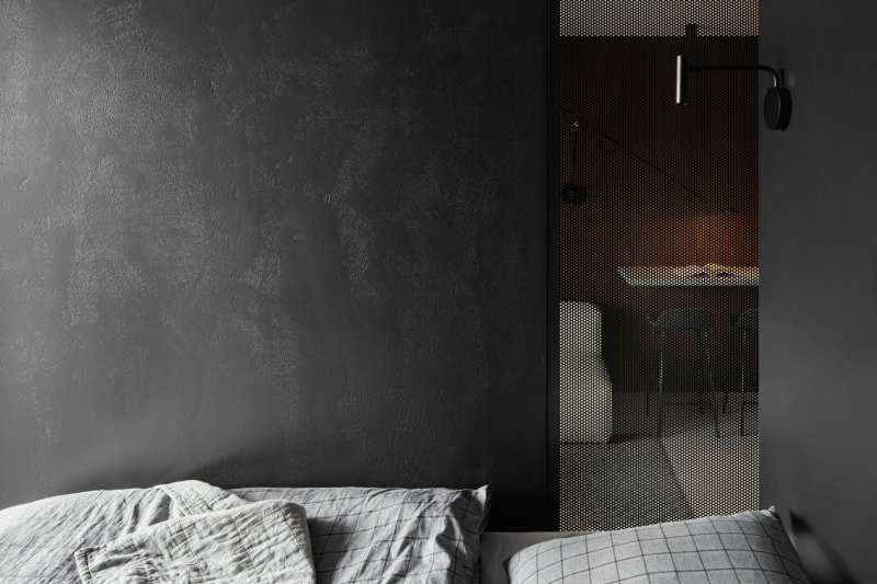 Ložnici od kuchyně s obývacím pokojem odděluje příčka s částí z perforovaného kovu. (Apartmán v Jizerských horách, MAVA ARCHI)