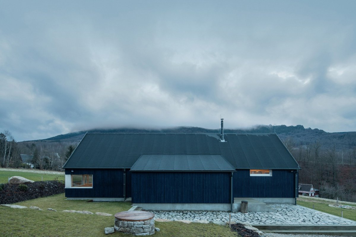 Chata v Jizerských horách, Markéta Cajthamlová, Architektonická projekční kancelář: Sokl domu je ze světlého pohledového betonu, fasáda pak z vertikálně kladeného prkenného obkladu v tmavě modré barvě