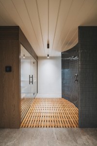 Součástí interiéru je také sauna s ochlazovací zónou, kde tmavé keramické obklady kontrastují se světlým dřevěným roštem a minimalistickým řešením prostoru. (Chalupa ve stráni; Mimosa Architekti)