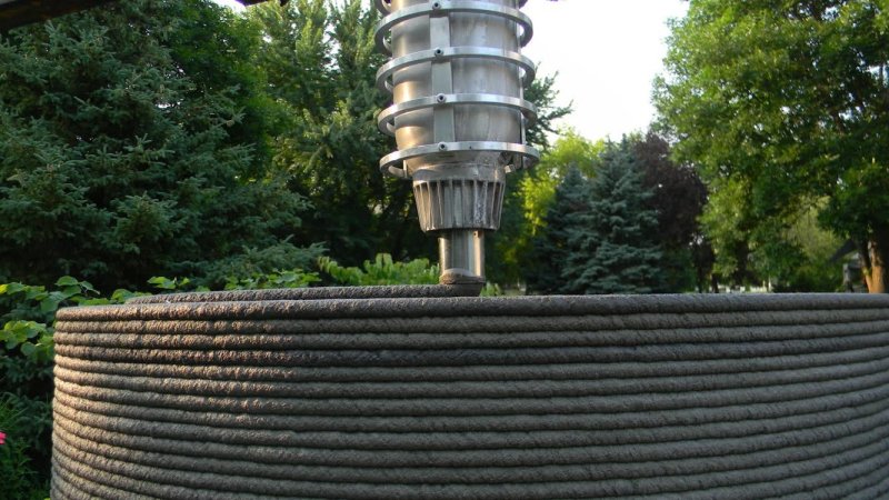 Obr. 16 Ukázka vytlačování cementové malty z tiskové hlavy a následné textury stěny realizované technologií 3D tisku vytlačováním cementové malty, Total Kustom, USA