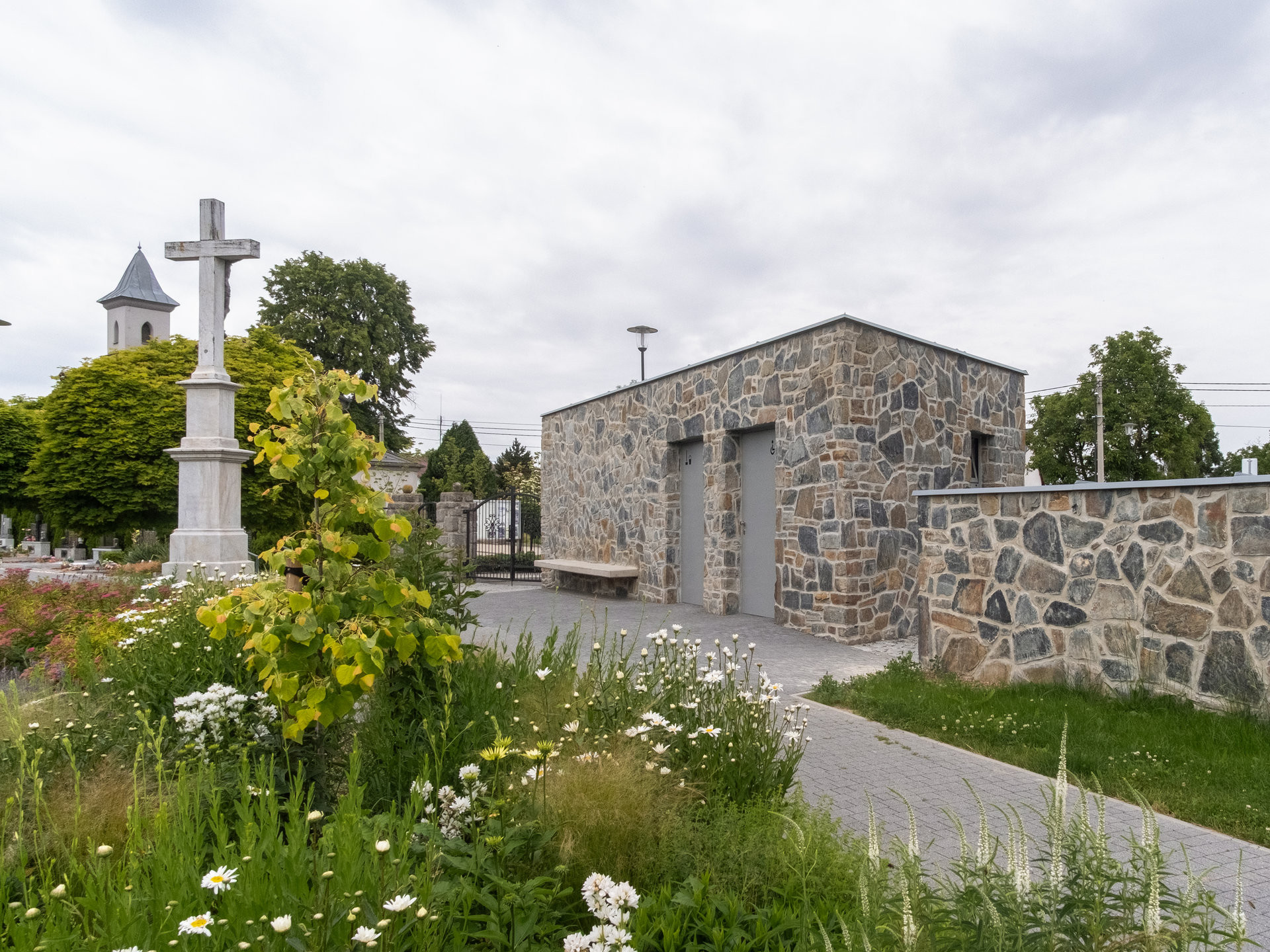 Zkultivovaný veřejný prostor kolem stávajícího kamenného kříže jako součást revitalizace. (Zázemí hřbitova; bydloarchitekti)