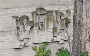 Reliéf umístěný na výrobní hale zobrazujicí dvě postavy u železobetonového panelu, jenž je zavěšen na jeřábovou kočku. Autor reliéfu neznámý.
