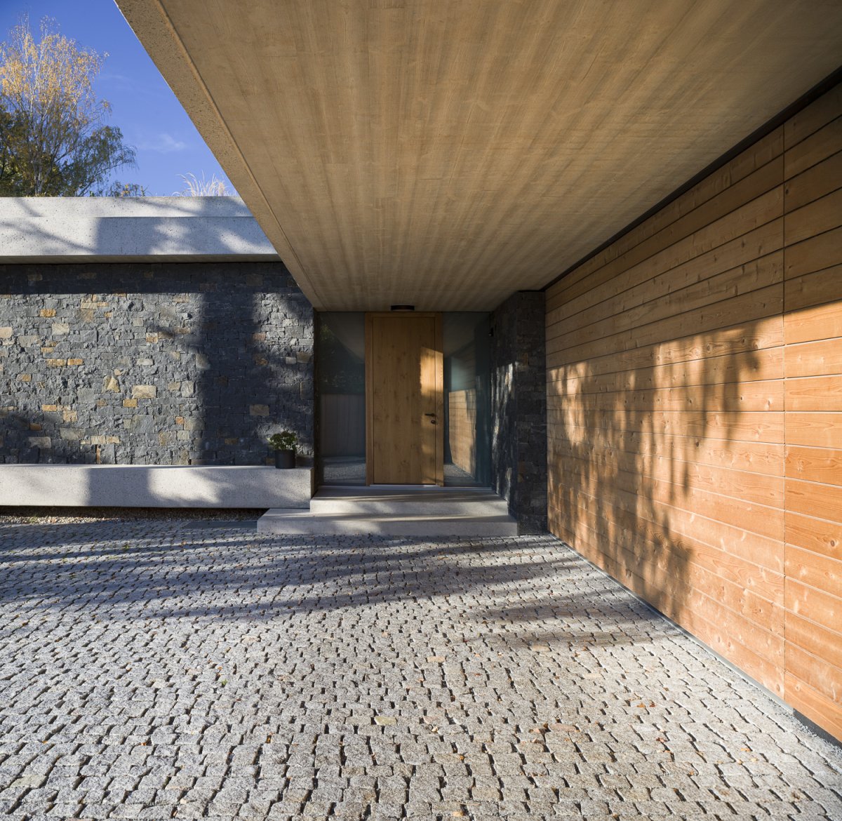 Škála materiálů je patrná už u vstupu: dřevo, beton, kámen. (Villa Lamella, A69 architekti)
