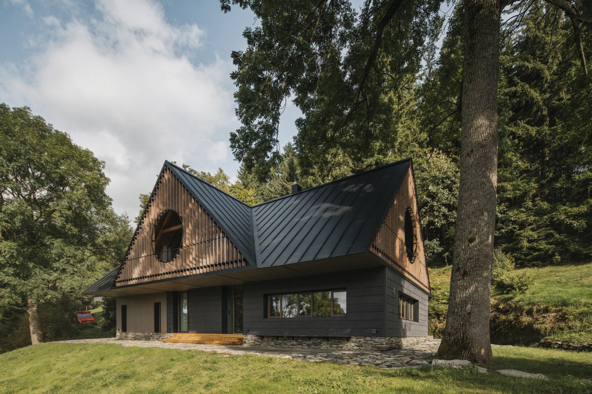 Dřevěná fasáda, kruhové vikýře a velkorysé prosklení propojují tradiční formu chalupy se současným architektonickým výrazem. (Chalupa ve stráni; Mimosa Architekti)