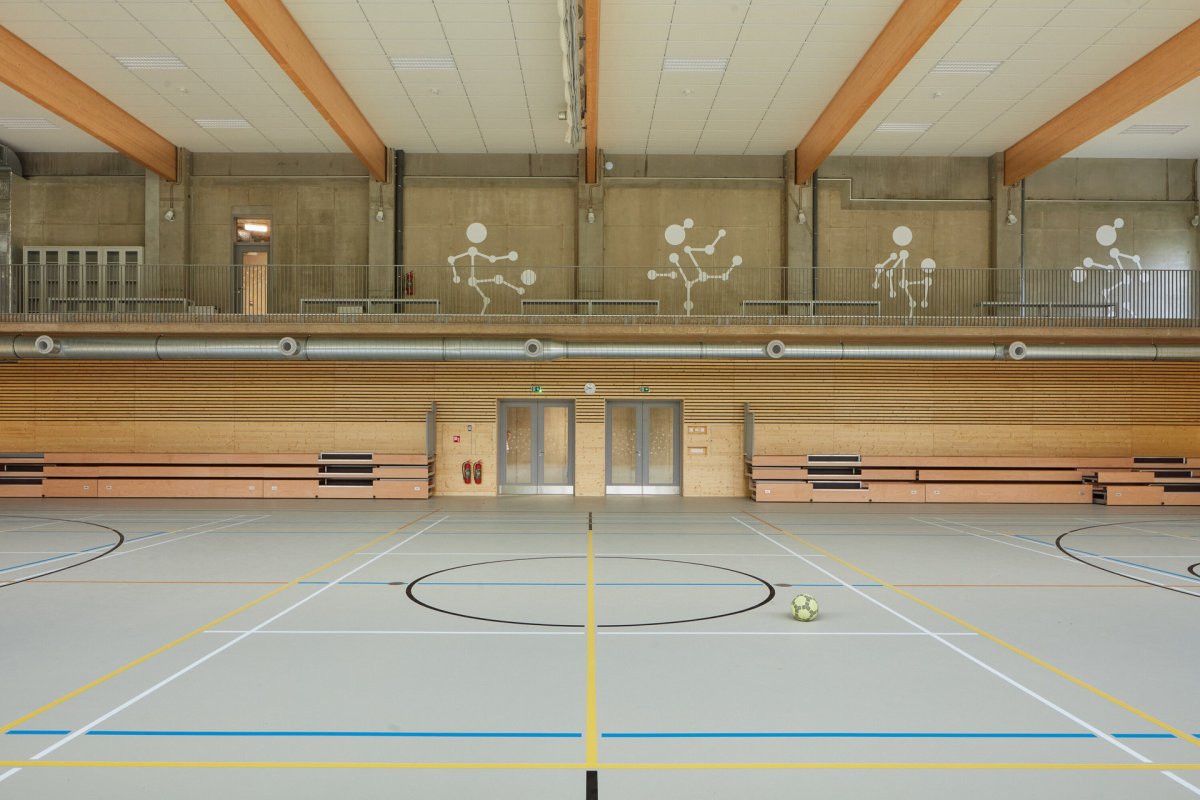 V tělocvičně dominují dřevěné prvky, pohledový beton a šedá podlaha s barevnými čárami pro různé sporty. (ZŠ bratří Fričů v Ondřejově; ATELIER 6)