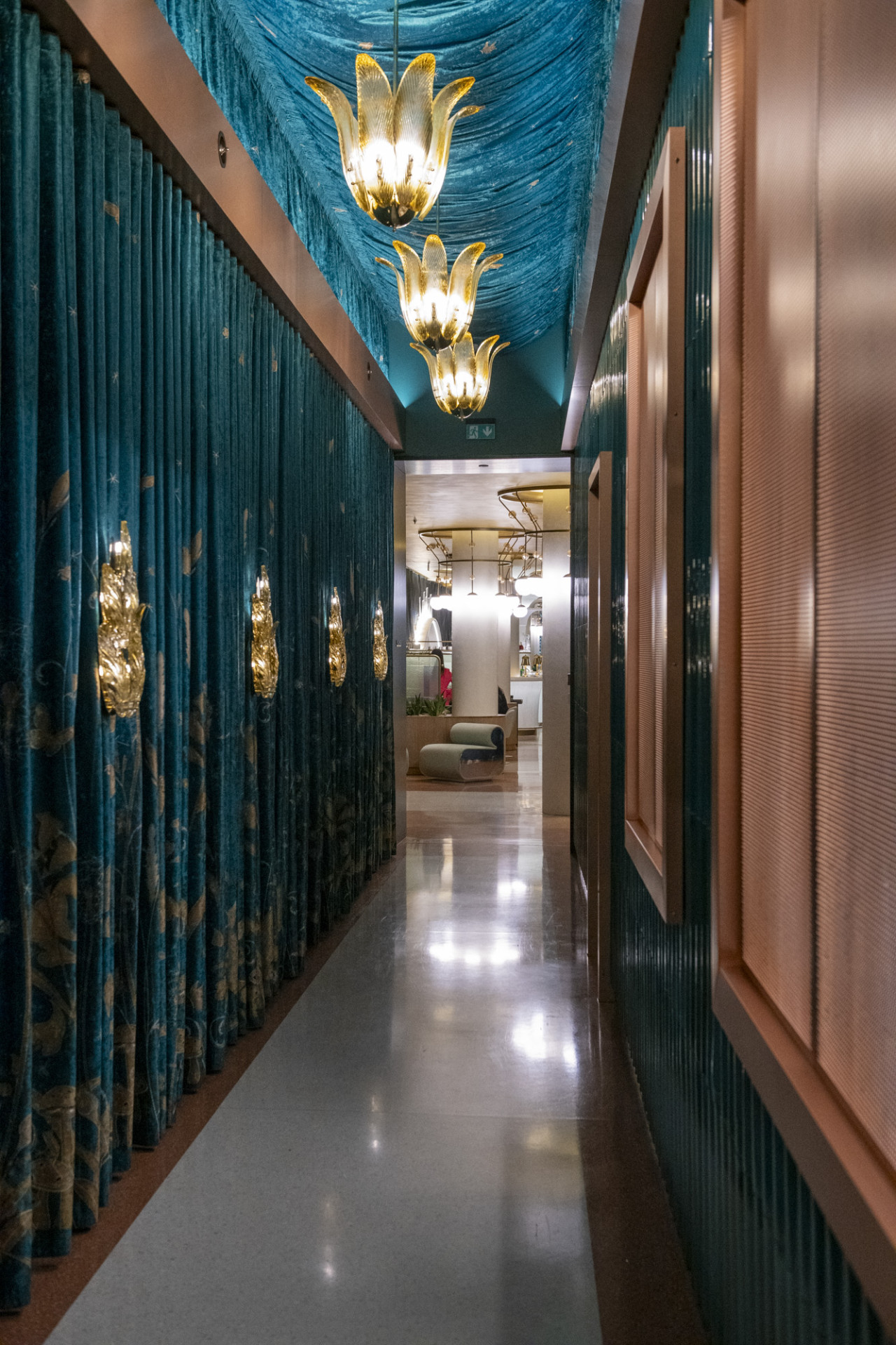 Historickou budovu hotelu a novou přístavbu spojuje tento průchod – ztvárněný, stejně jako všechny interiéry v hotelu, pompézně. Perforovanými plechy na stěně po pravé straně je dokonce vidět do kuchyně, přímo pod ruce kuchařského týmu.