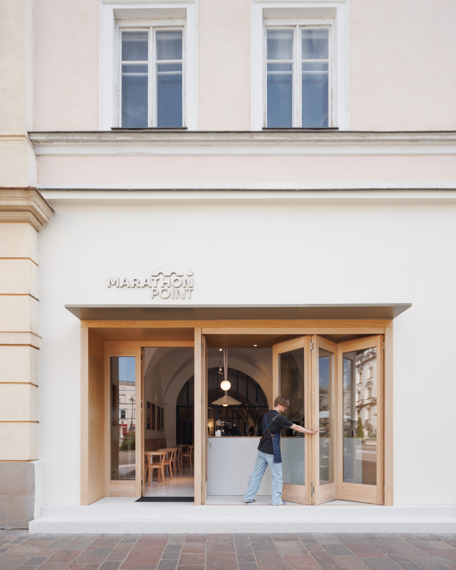 „Otevření do veřejného prostoru hraje ústřední roli,“ popisuje architekt klíčový princip, podpořený skládacími vstupními dveřmi ústícími na hlavní korzo. Prostor tematicky leží přímo na původní trase v centru města a odkazuje na občerstvovací stanice. 