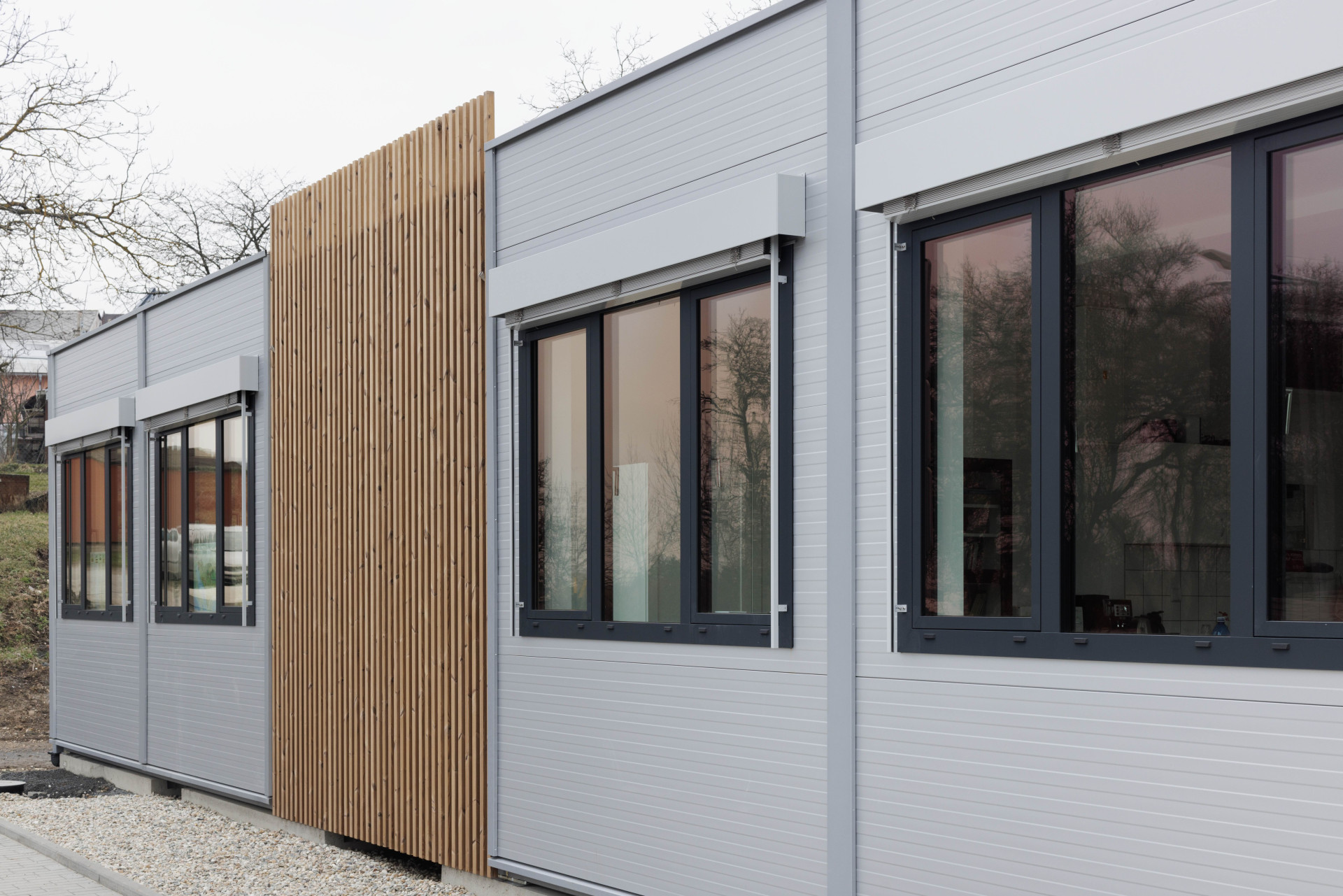 Moderní vzhled dodává stavbě použití elegantních šedých PUR panelů, velkých hliníkových oken a venkovních žaluzií. (ZŠ Drahanovice od společnosti KOMA)