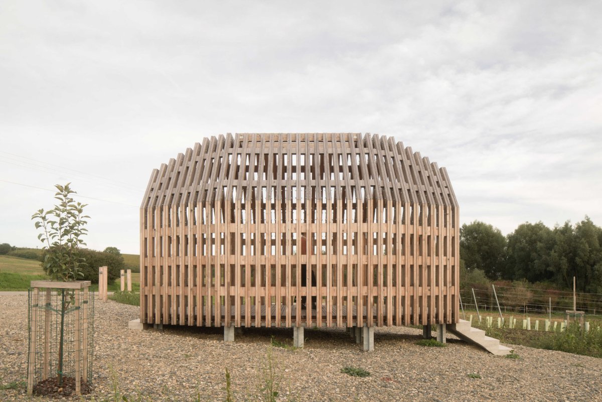 Kaple je vzdušná a průchozí, rámuje vchod do celého agrovoltaického areálu.