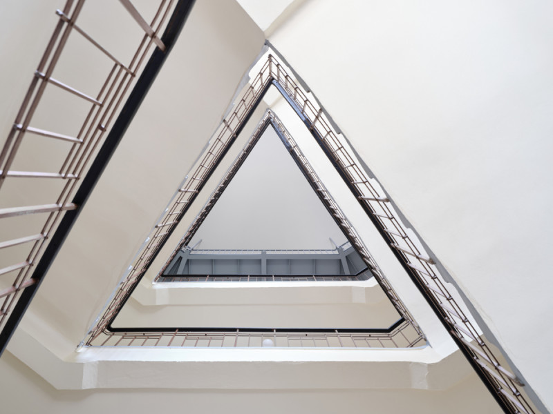 Průhled zachovalým volným zrcadlem kamenného schodiště bytového domu. (Nástavba Harfa; matěj šebek architekti)