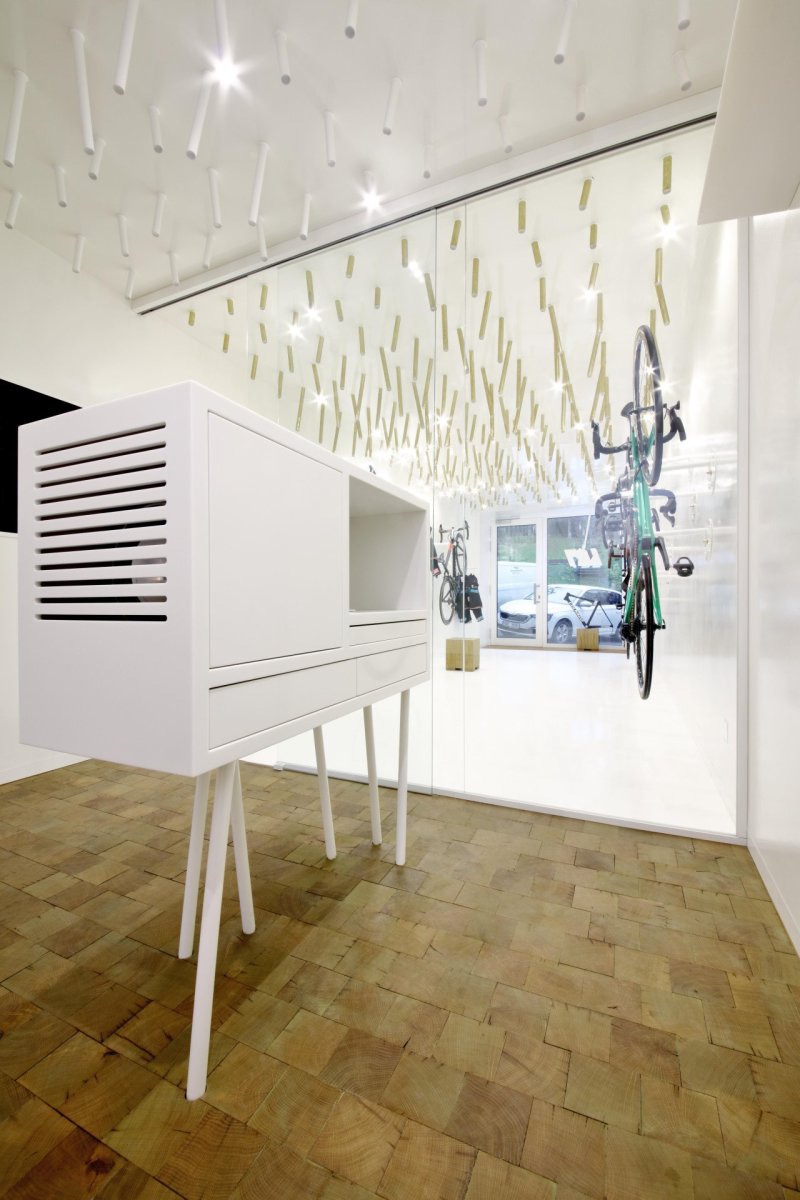 Cyklobutik L27, P6PA+Architects: Špalíková dlažba ošetřená voskem kontrastuje s bílou podlahou v přední části