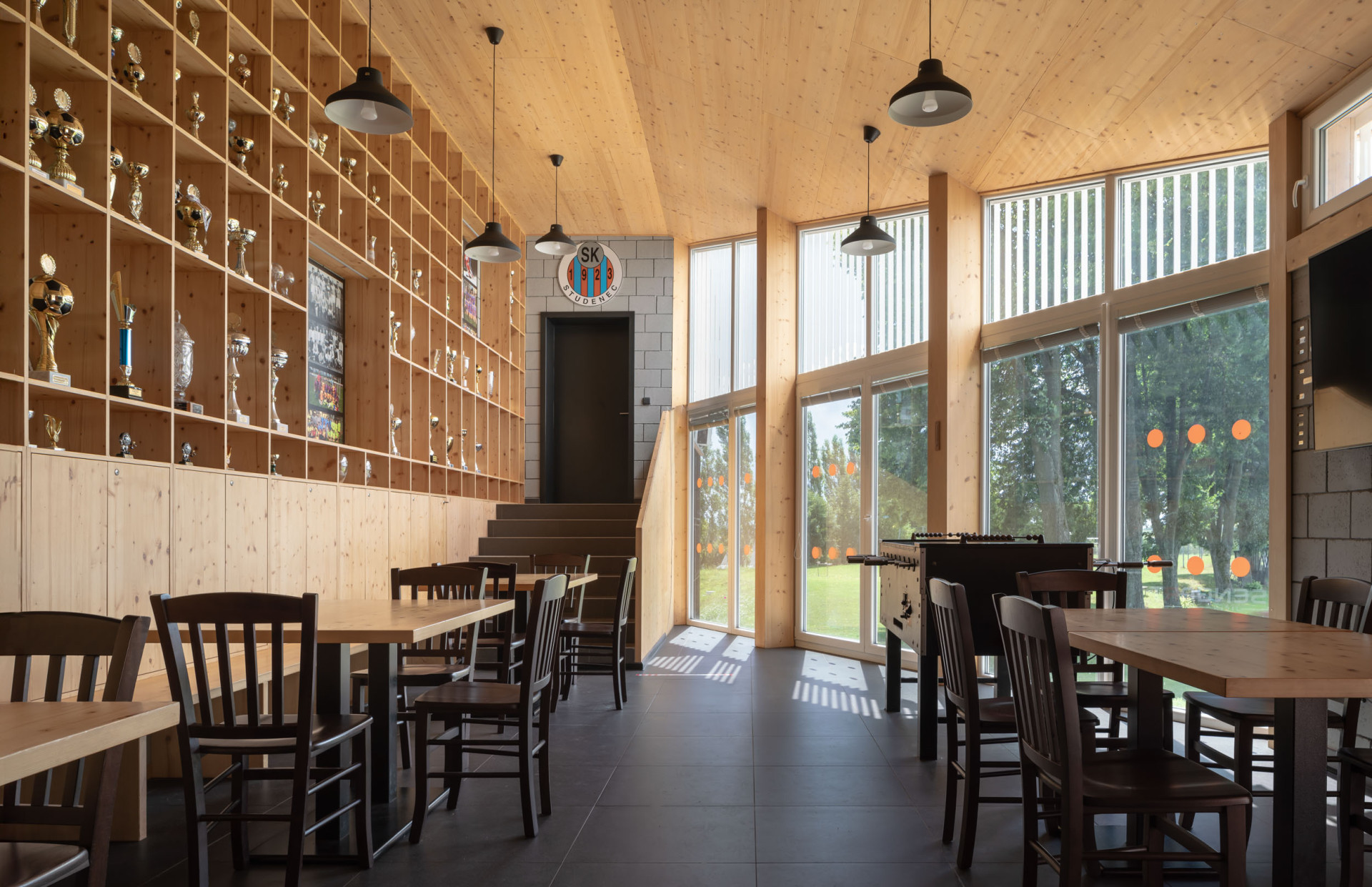 Směrem ven se otevírá prosklenou stěnou. (Zázemí sportovního klubu ve Studenci, ateliér CHRAMA)