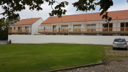 Komunitní dům pro seniory v Holasovicích, City Upgrade: Stavba se otevírá do čtvercového dvora, kde stojí taky památkově chráněná sýpka. Směřují k ní zavěšené balkony a soukromé zahrádky