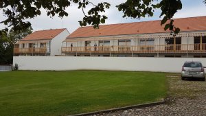 Komunitní dům pro seniory v Holasovicích, City Upgrade: Stavba se otevírá do čtvercového dvora, kde stojí taky památkově chráněná sýpka. Směřují k ní zavěšené balkony a soukromé zahrádky