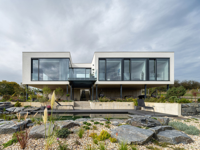 Hlavní obytný trakt vily je vysunutý nad terén a podpírají ho štíhlé ocelové sloupy. (Vila u Prahy, boq architekti)