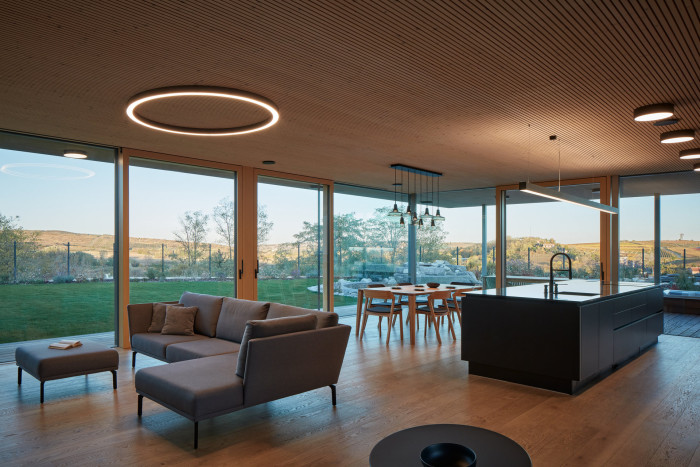 Akustické panely NOVATOP ACOUSTIC na stropě v Rodinném domě v Modrých Horách, které přecházejí přes bezrámová okna z interiéru do podhledu a přesahují do exteriéru.