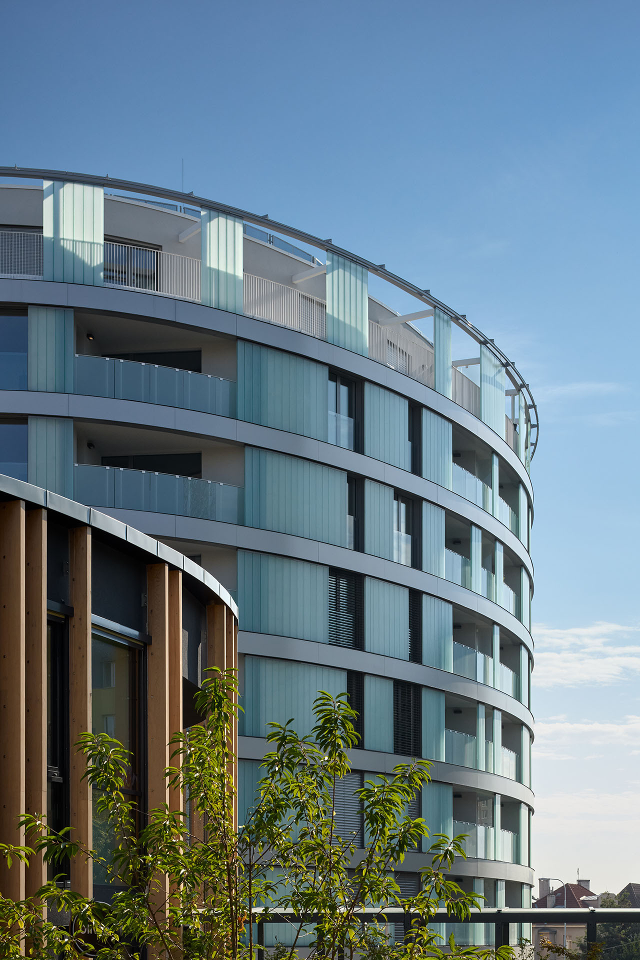 Fasáda domu je z matného skla, fasáda školky z dřevených latí. (Bytový dům Oliva, A69 architekti)