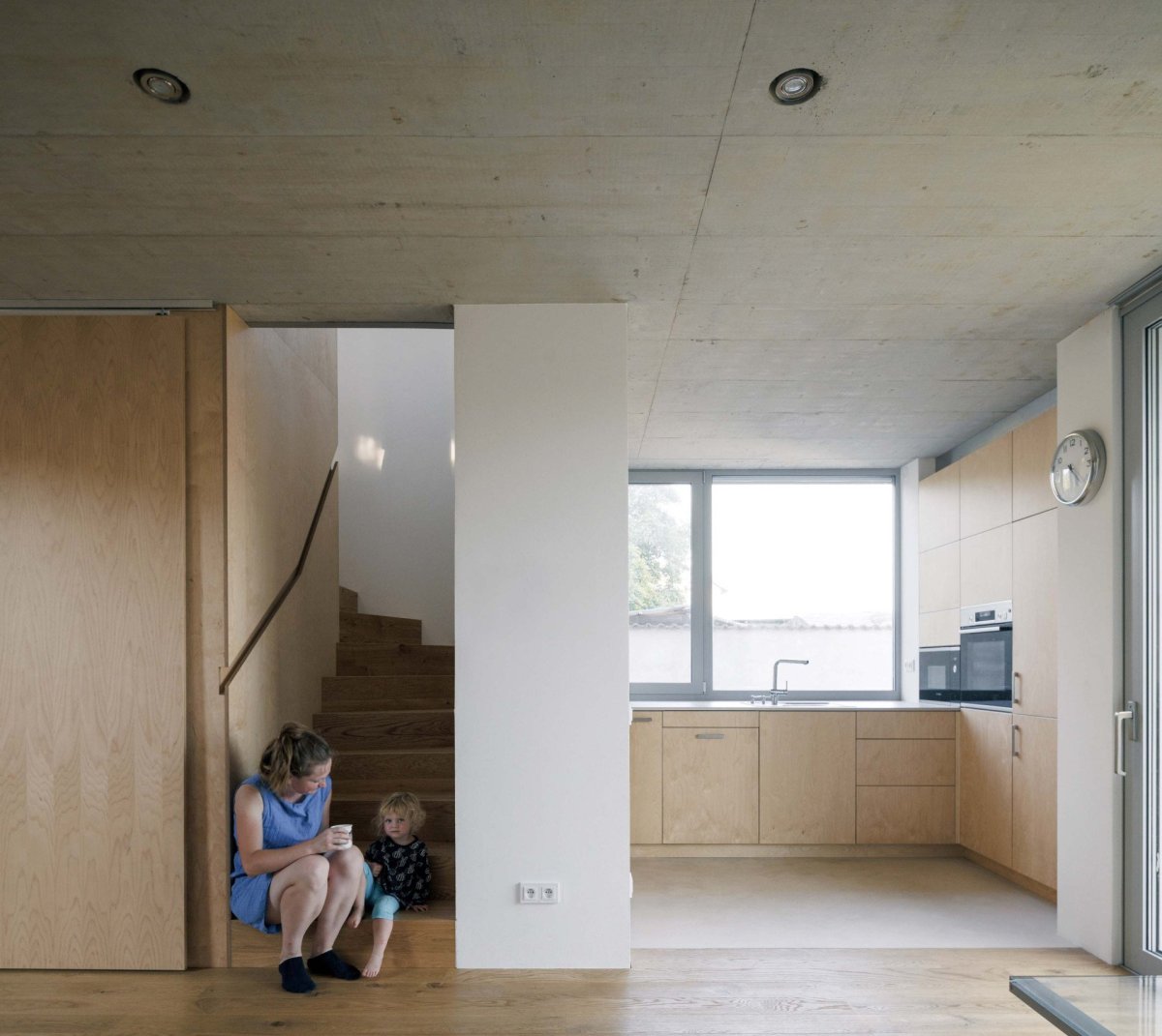 Schodišťový prostor je oddělitelný posuvnými dveřmi od obývacího pokoje. (Rodinný dům v Radotíně, Papundekl architekti)