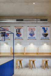 S kostičkami se v interiéru pracuje hlavně ve 2D formátu. Stěny pokrývají bílé obkladačky s modrými a červenými spárami. (Bistro Ramencraft v Praze, SAO Architekti)